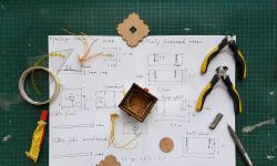 Tools, glue and piece of a prototyped box on a sheet of paper with drawing and dimensions